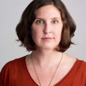 Headshot of Ann Marie wearing an orange shirt and a silver necklace. She is a white woman with chin length short brown hair.