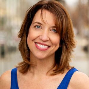 This photo is of Christina Lazo. She is a white woman with brown hair and blue eyes. In the photos she is smiling, and wearing a blue tank top. The background image is blurred out to focus on the image of her.