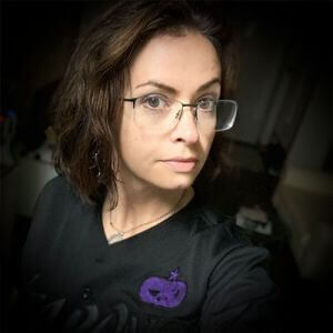 A headshot of a woman with dark hair and glasses, wearing black.