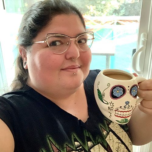 Woman wearing glasses holding coffee cup painted to look like a sugar skull.