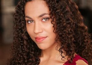 Headshot of Aidaa Peerzada. A medium skinned woman with medium length curly brown hair and hazel eyes. She is wearing a red lace tank top.