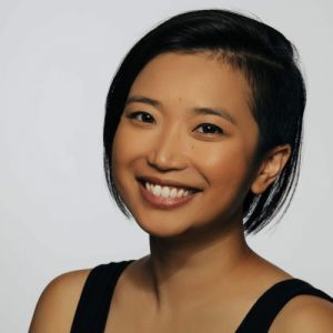 Headshot of an Asian American woman of Filipino and Chinese descent. She is smiling in front of a white background. She has a black bob haircut and is wearing a black tank top.